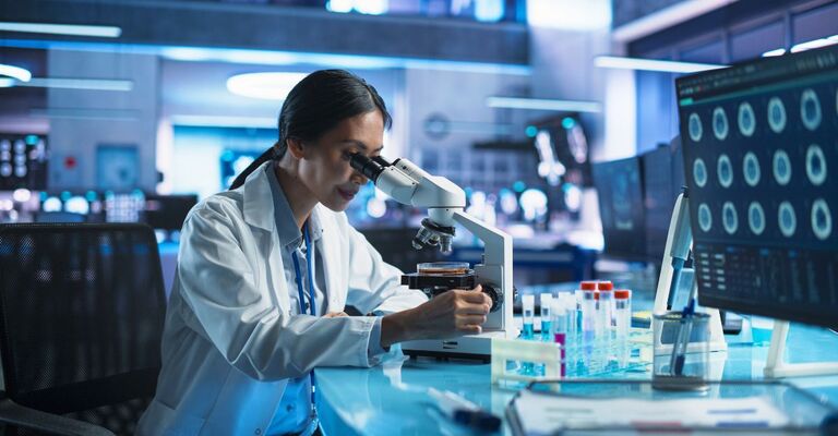 Laboratorio di sviluppo di farmaci: una scienziata asiatica analizza un campione in una piastra di Petri al microscopio. Ricerche biotecnologiche e sviluppo di nuovi farmaci.