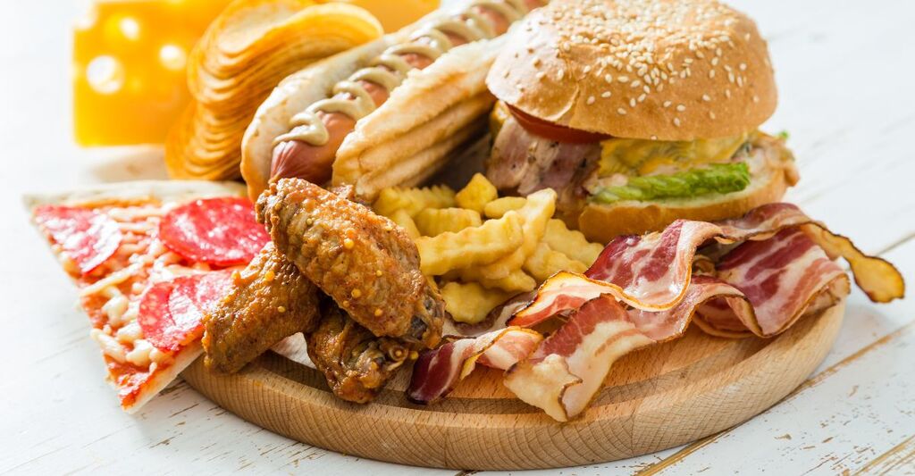 Piatto con cibi ultra-processati tra cui pizza, ali di pollo, hamburger, hot dog, pancetta e patatine fritte.