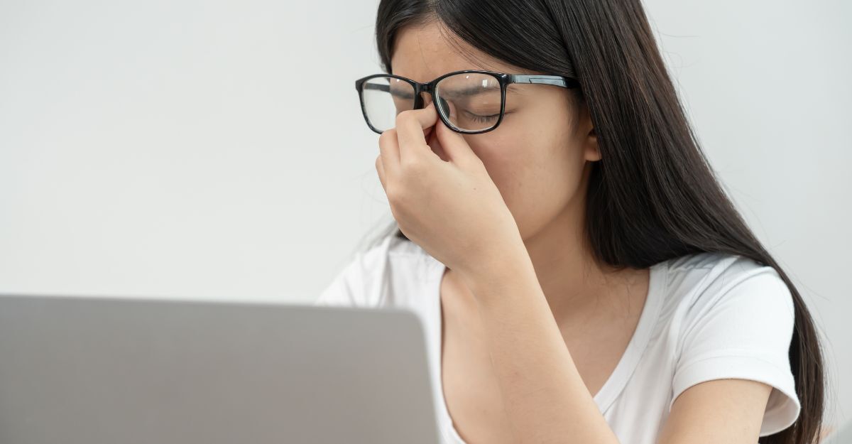 Persona con occhiali si tocca il ponte del naso davanti a un computer.