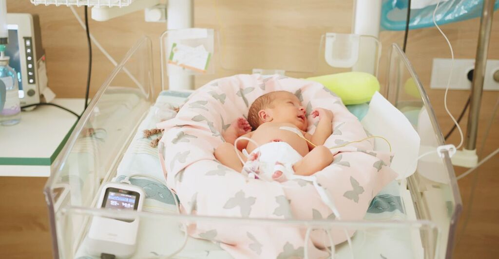 Neonato che riposa in un'incubatrice ospedaliera. Il neonato è monitorato e riceve cure mediche. Rappresenta la terapia intensiva neonatale.