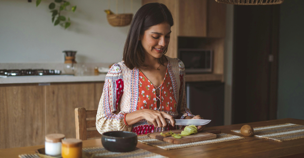PCOS e insulino-resistenza: la guida della nutrizionista a sintomi e dieta Giovane donna in cucina che prepara la sua colazione. Taglia dei kiwi su un tagliere in legno