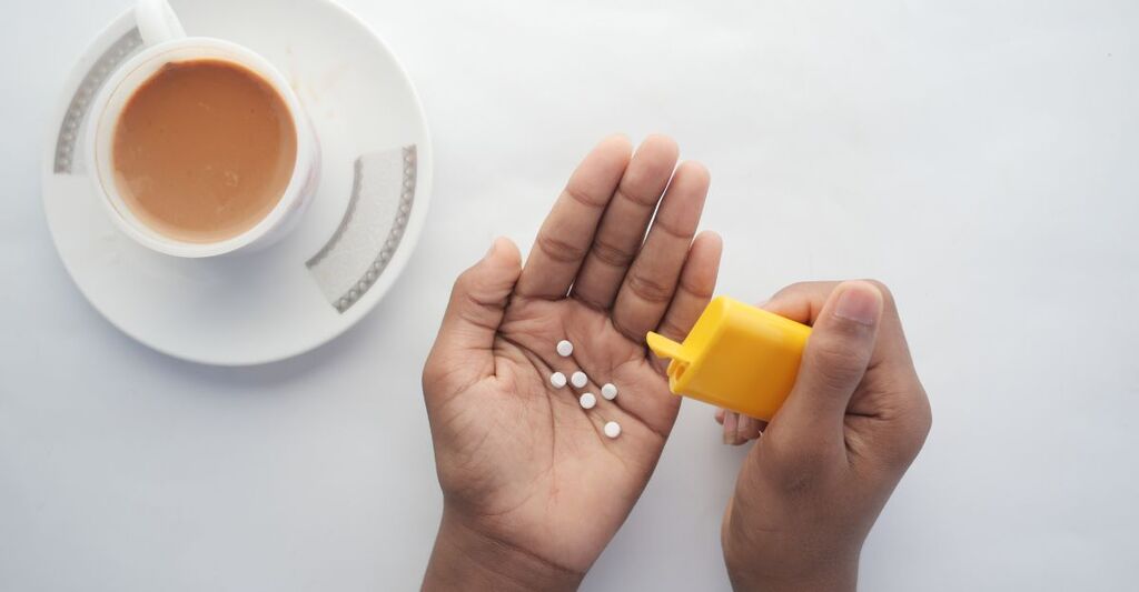 Una tazzina di caffè e una mano che tiene i dolcificanti.