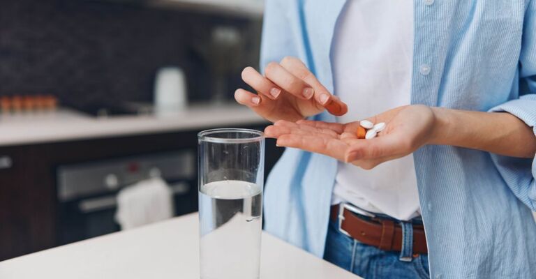 Donna che tiene una pillola in mano e si prepara a prendere il farmaco con un bicchiere d'acqua