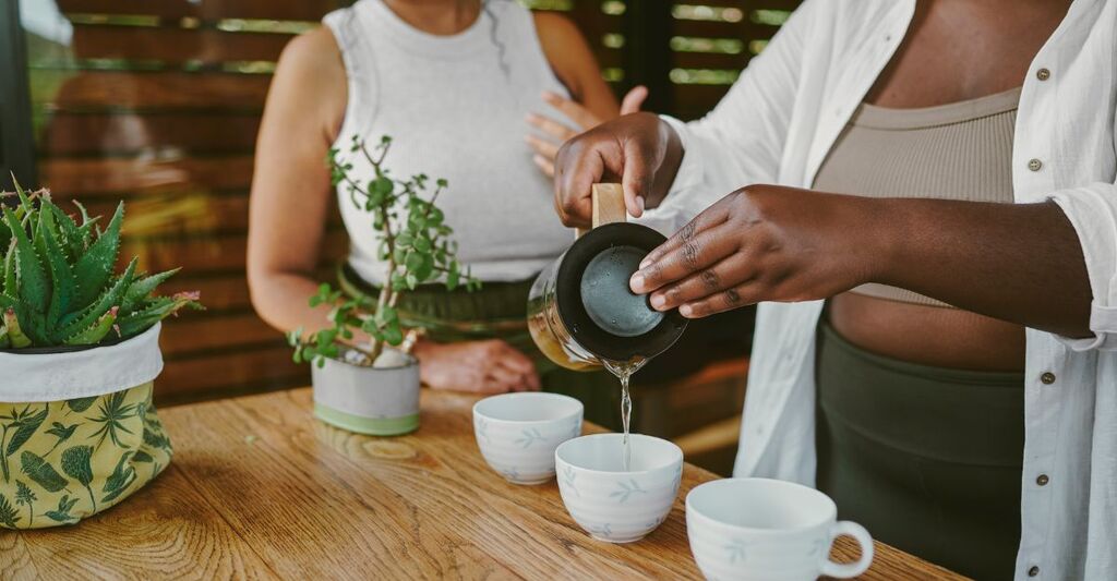 Persona che versa un infuso in tazzine su un tavolo di legno.