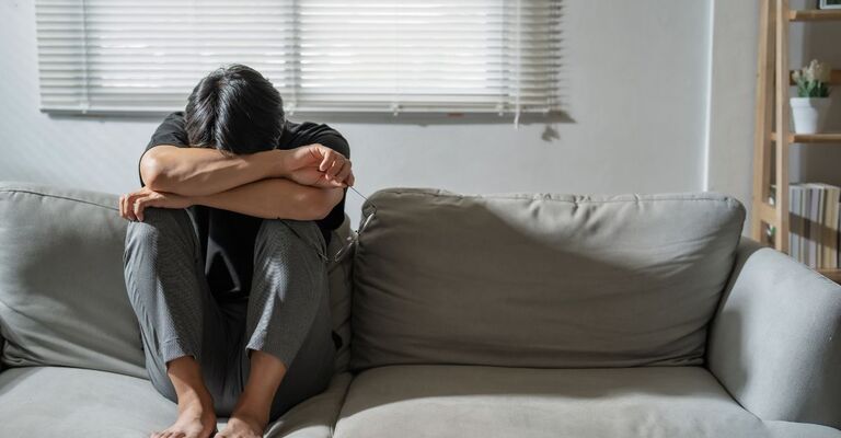 Il meccanismo cerebrale che spegne l’ansia Persona seduta su un divano, testa tra le ginocchia, in posizione di sconforto o depressione.