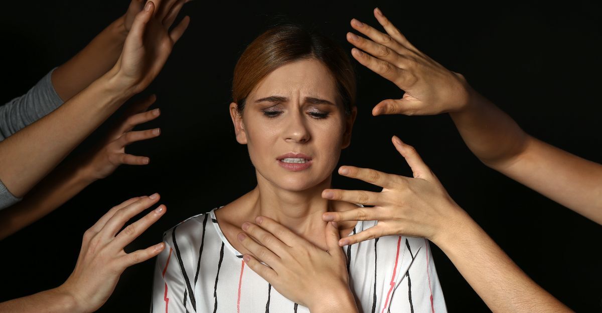 Donna in difficoltà con espressione di ansia o panico, circondata da mani tese.