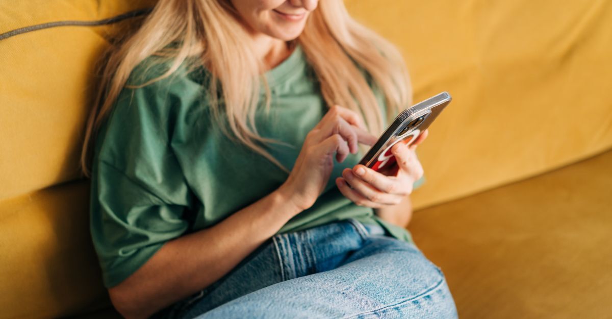 Una donna irriconoscibile naviga sui social media con il cellulare mentre è seduta sul divano giallo di casa