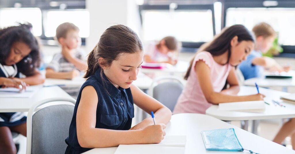 Primo piano di bambine e bambini in classe. Stanno scrivendo sui quaderni e sembrano concentrati