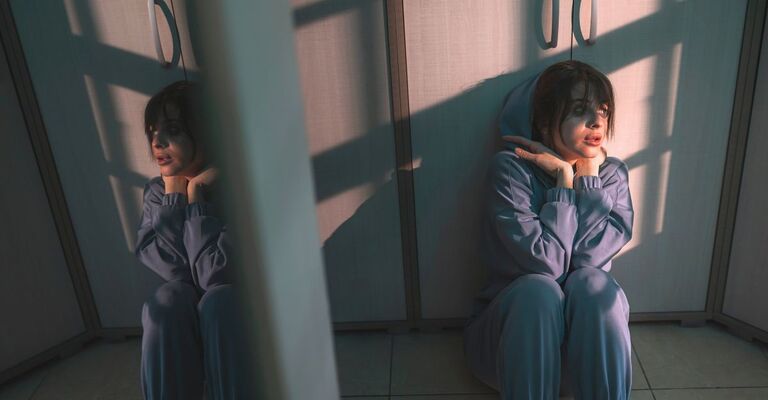 Sentire le voci e schizofrenia Una donna con schizofrenia seduta a terra in una stanza.