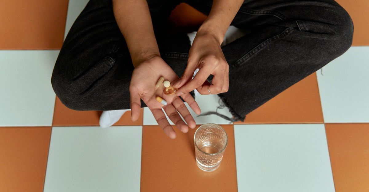 Lattoferrina: dove si trova e quali sono le fonti naturali e integrative Primo piano di una ragazza seduta per terra a a gambe incrociate. Ha in mano delle compresse e c'è un bicchiere sul pavimento