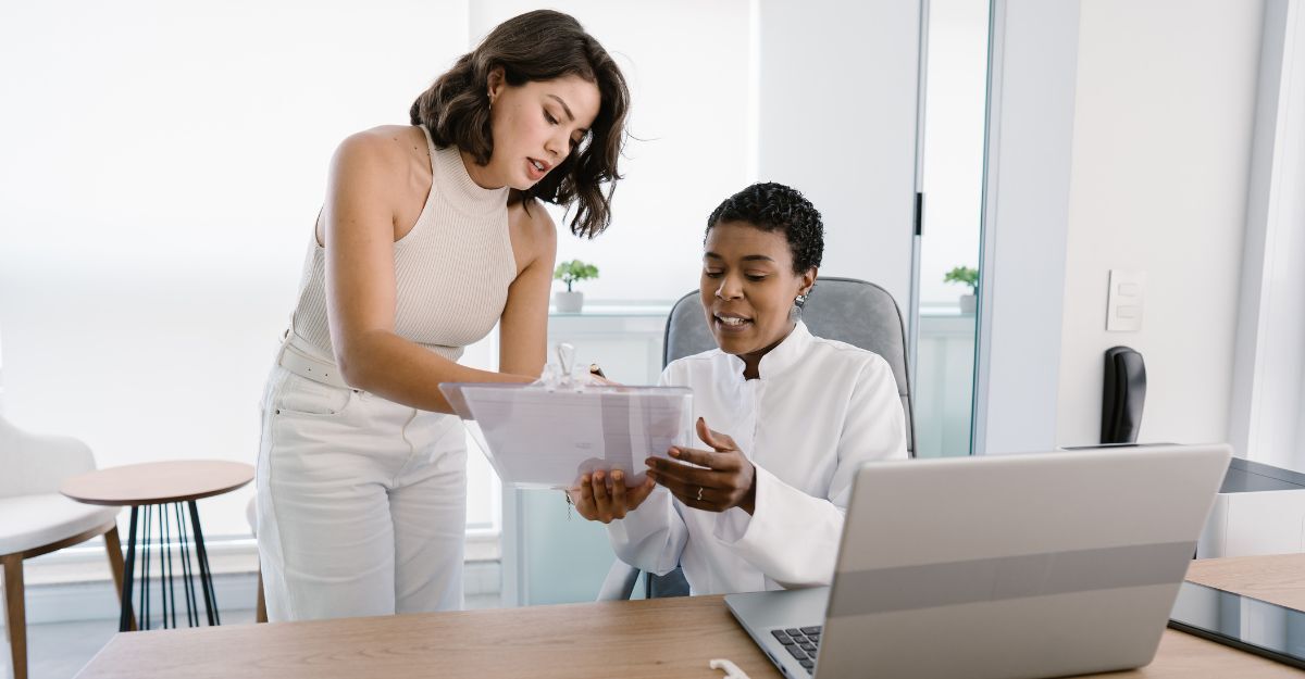 Due donne professioniste sanitarie esaminano dei documenti su una tavoletta digitale in ufficio.