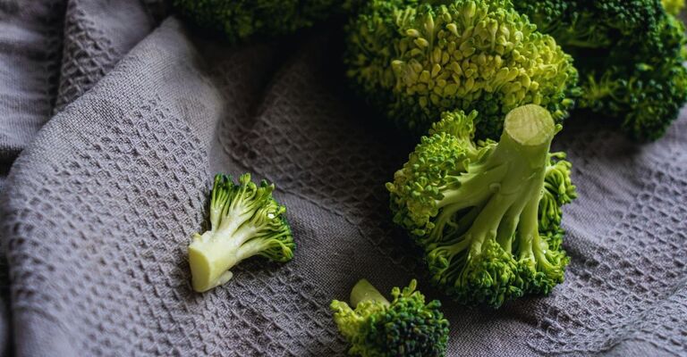 Proprietà dei broccoli: benefici, valori nutrizionali e come consumarli al meglio Primo bianco di un canovaccio lilla con broccoli crudi adagiati sopra