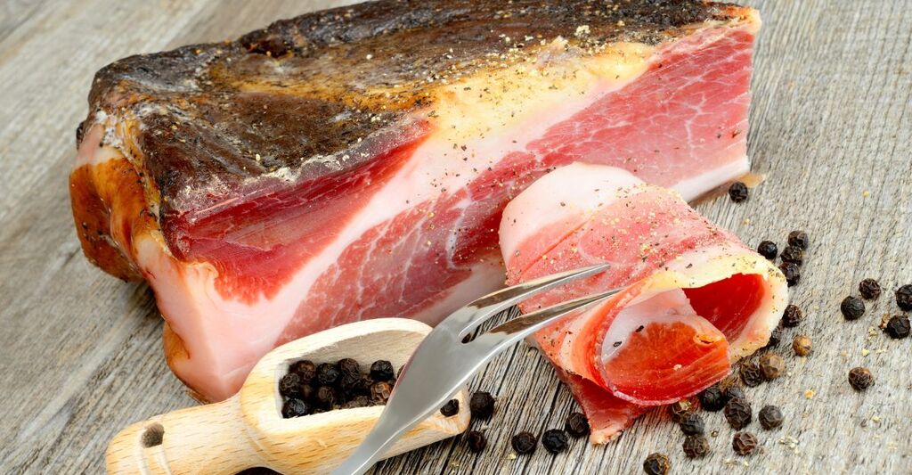Pezzo di speck su un tagliere di legno.