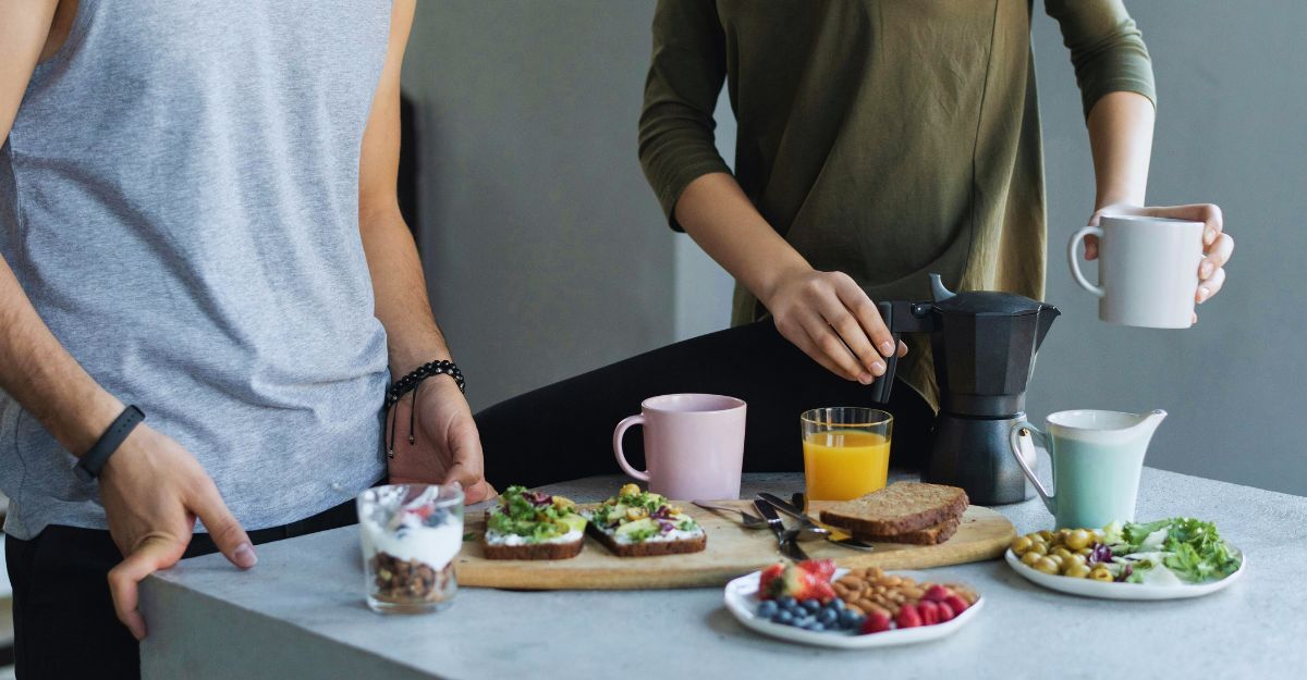 Saltare la colazione potrebbe aumentare il rischio di sindrome metabolica Primo piano di due persone che fanno colazione con bevande calde, fredde e cibo sull'isola della cucina