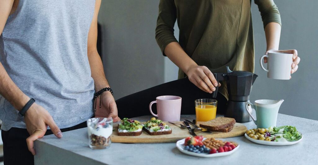 Primo piano di due persone che fanno colazione con bevande calde, fredde e cibo sull'isola della cucina
