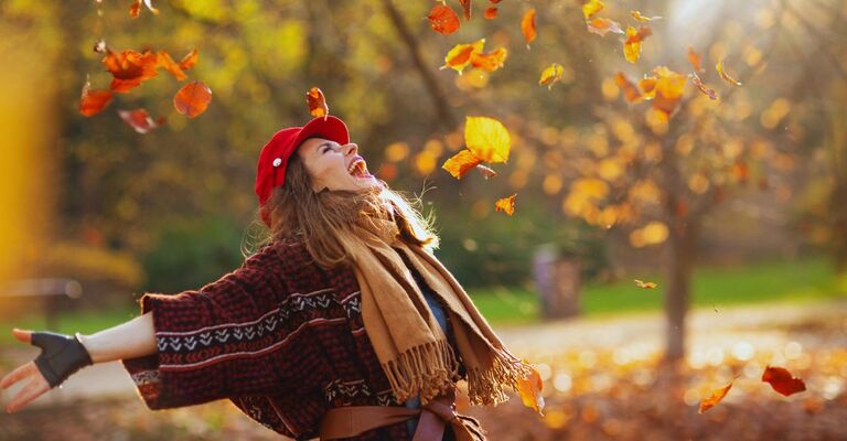 Come aumentare subito le difese immunitarie con il cambio di stagione Una donna con difese immunitarie alte immersa nelle foglie d'autunno.