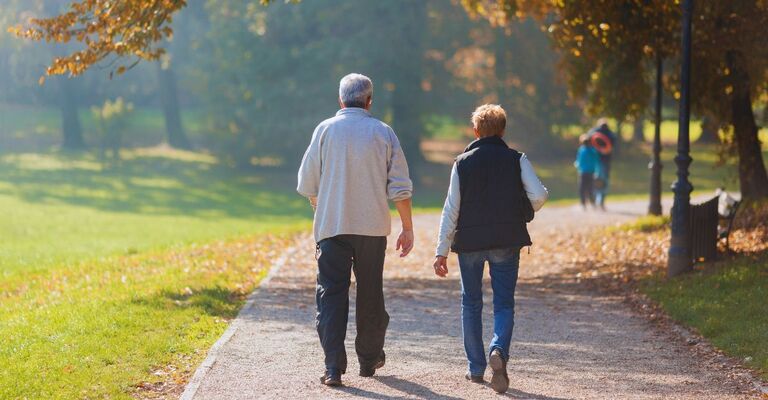Una coppia di anziani cammina in autunno in un parco con una giornata di sole