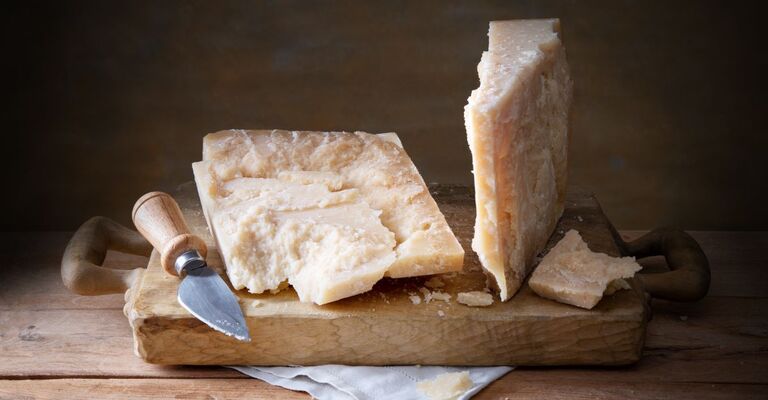 Parmigiano questo formaggio stagionato può far salire la glicemia Pezzi di parmigiano con coltello per formaggio duro su un tagliere di legno, spazio per il testo, primo piano.