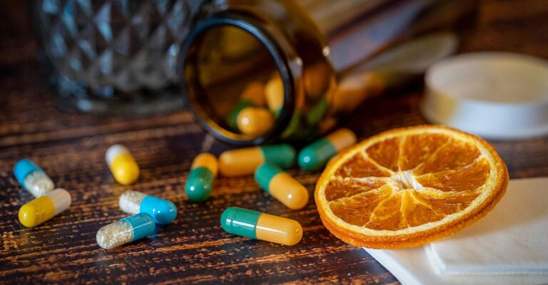 Capsule colorate e una fetta d'arancia su un tavolo di legno.