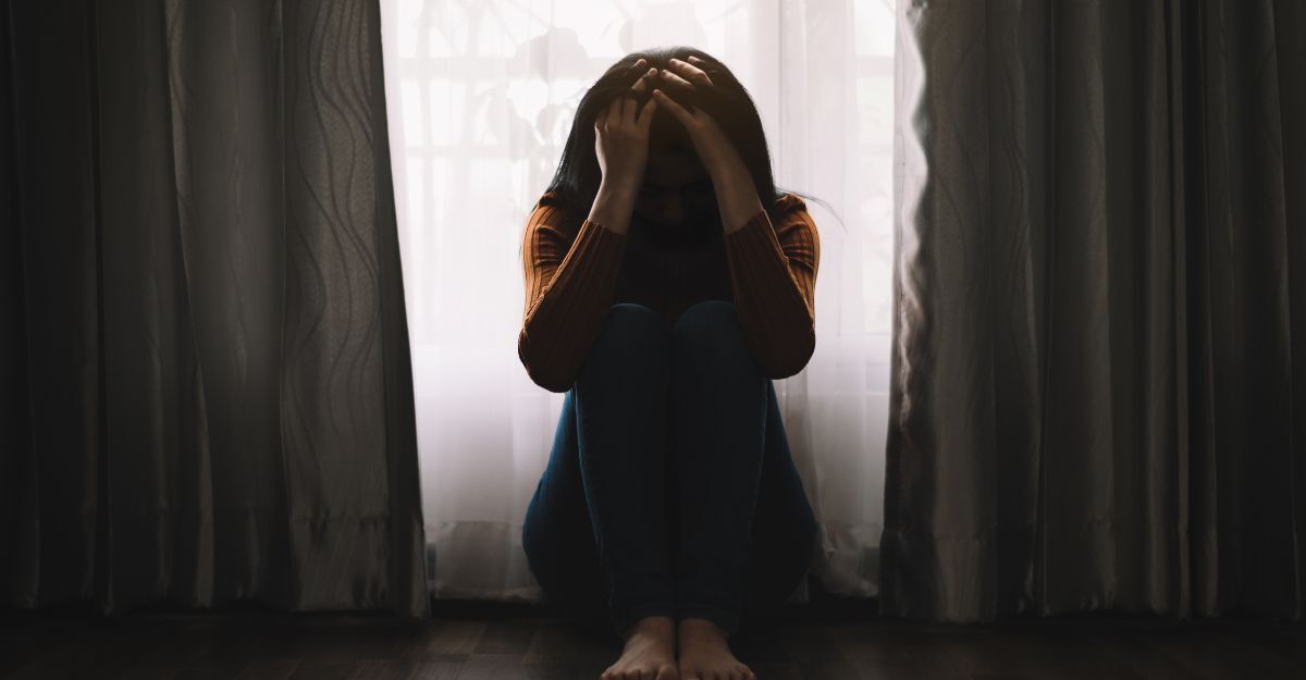 Donna seduta sul pavimento con le mani sulla testa.