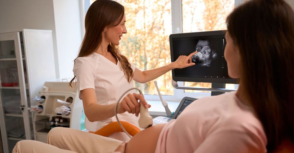 Donna incinta sottoposta a ecografia che osserva il monitor mentre la ginecologa indica