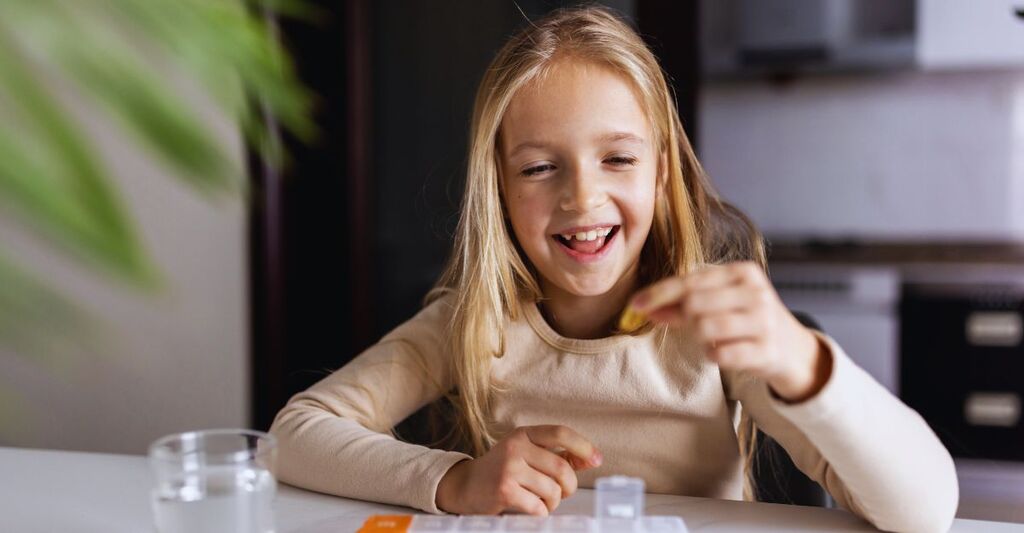 Una bambina caucasica in pigiama assume vitamina omega-3 naturale da una scatola di plastica in cucina a casa la mattina presto. Una bambina adorabile prende degli integratori.