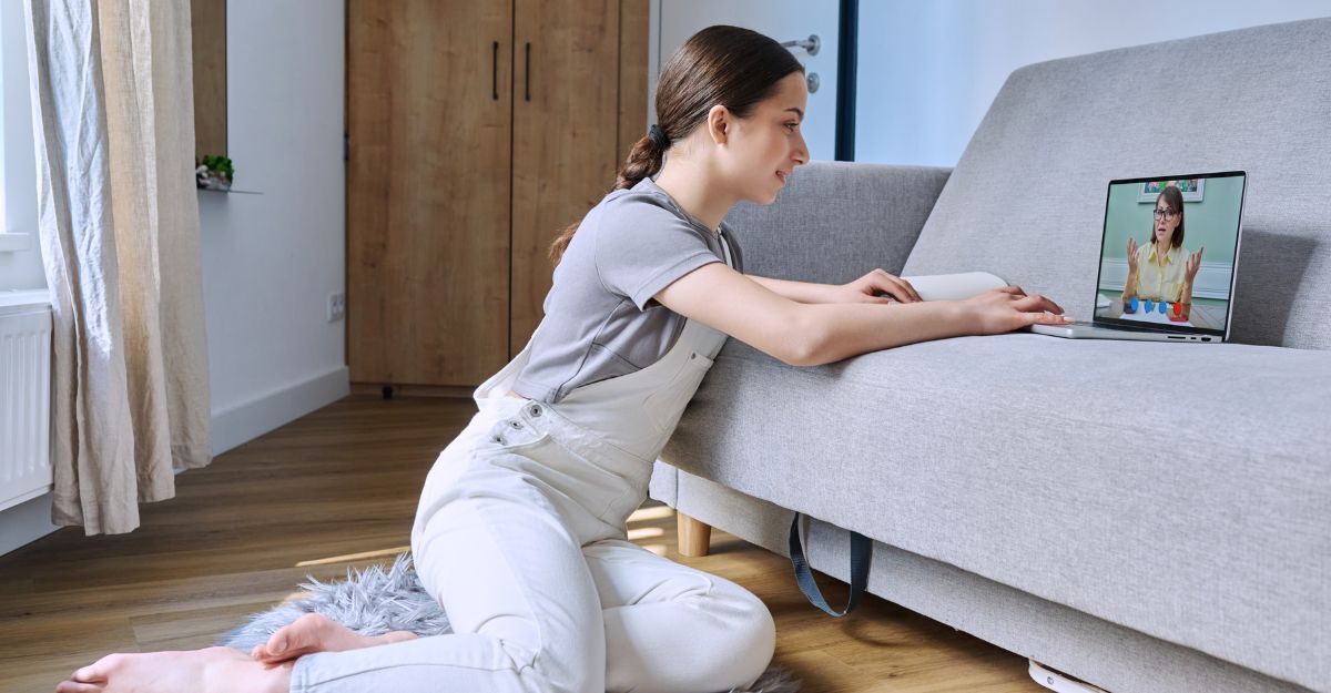 Ragazza seduta sul pavimento di casa che segue una sessione di teleterapia su laptop.