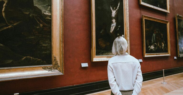 Donna di spalle che osserva dei quadri a olio in un museo