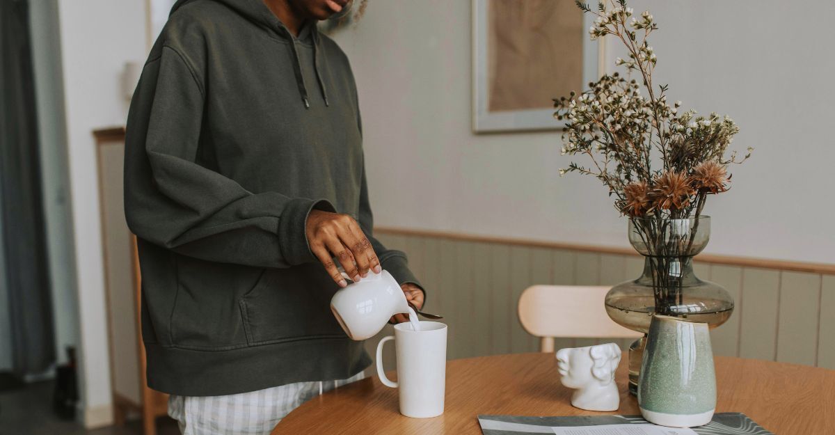 Primo piano di un ragazzo che versa del latto da un bricchetto dentro la tazza sul tavolo del soggiorno