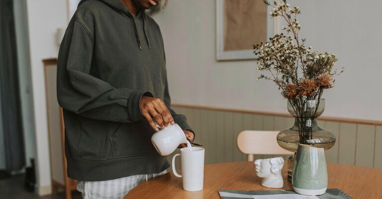 Primo piano di un ragazzo che versa del latto da un bricchetto dentro la tazza sul tavolo del soggiorno