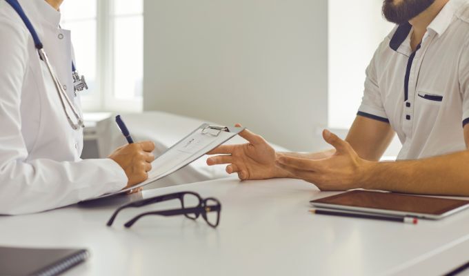 Medico prende appunti parlando con un paziente.