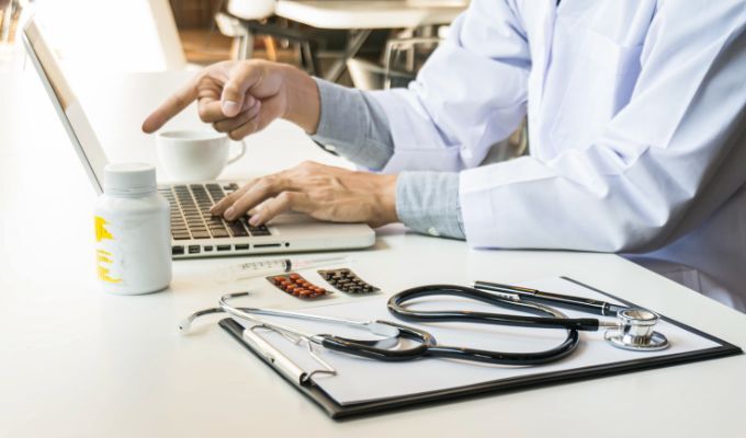 Medico lavora al laptop con stetoscopio e farmaci.