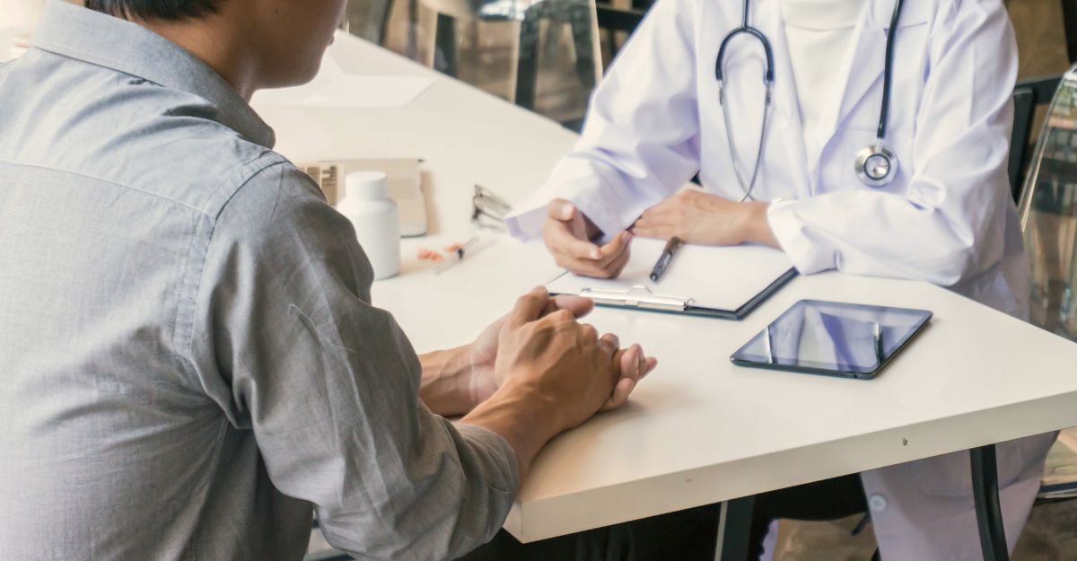 Paziente seduto di fronte a un medico che indossa un camice bianco, durante una consultazione.