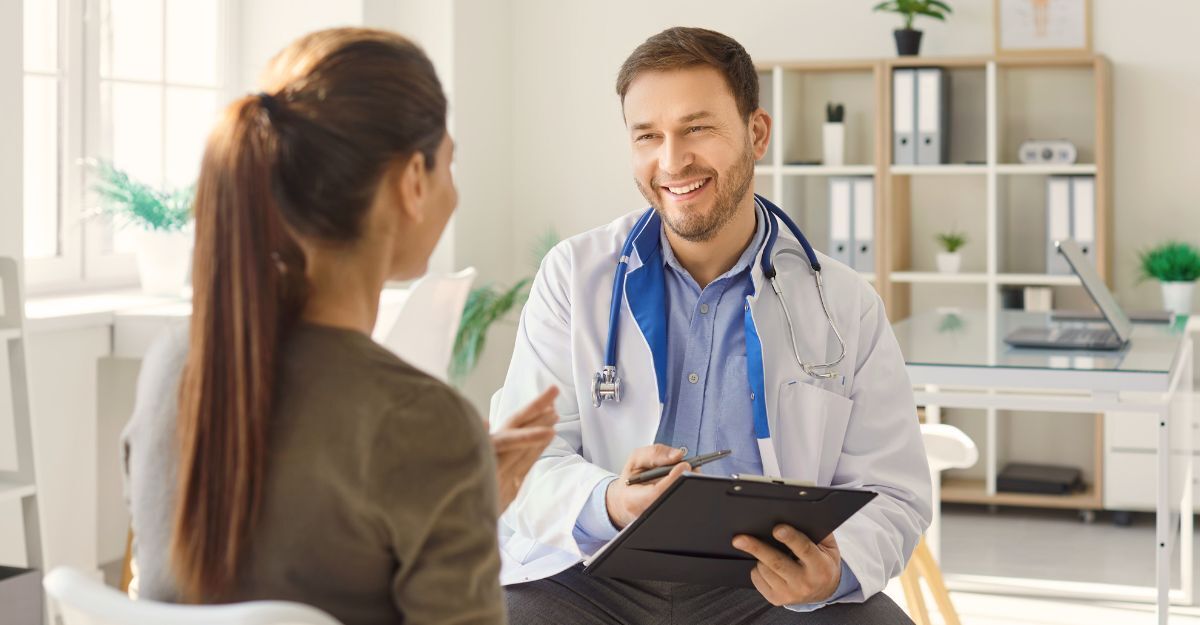 Medico sorridente seduto con un paziente, prendendo appunti su una cartella clinica.