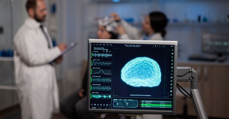 Monitor con attività cerebrale sullo schermo in un laboratorio medico di neurologia. Sullo sfondo, un team di neurologi regola le cuffie EEG di una paziente che monitora il sistema nervoso durante un esperimento neuroscientifico