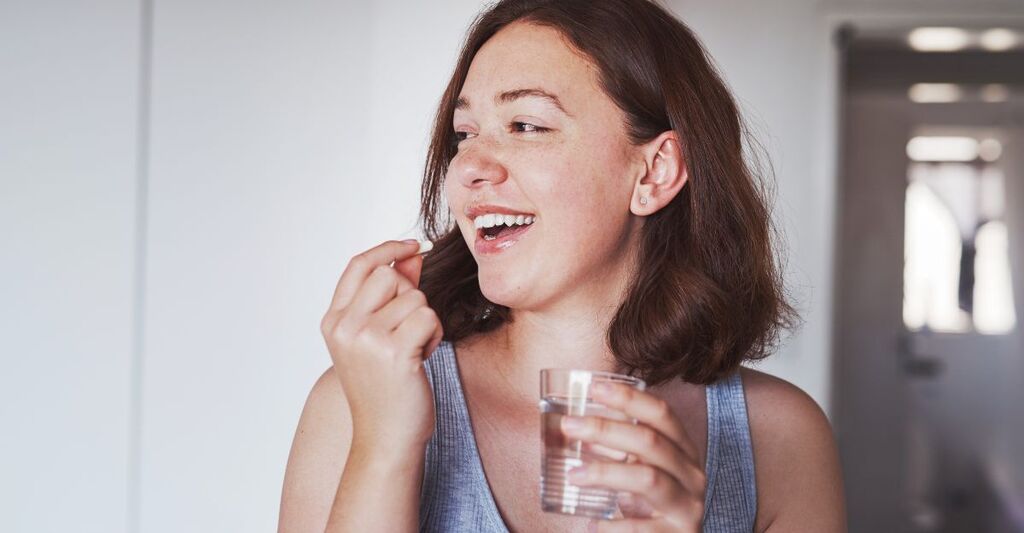 Assistenza sanitaria, farmaci e una donna che beve una pillola con un bicchiere d'acqua per il benessere a casa sua. Medicina, medicina e una donna felice che prende una vitamina, un integratore o una compressa con un liquido in appartamento.