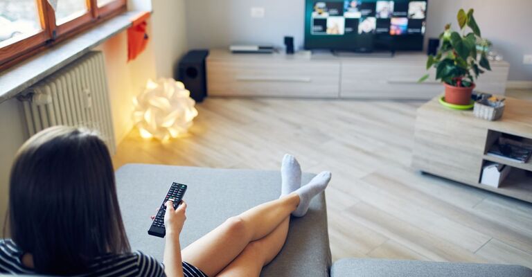 Giovane ragazza con telecomando guarda la tv in salotto seduta sul divano