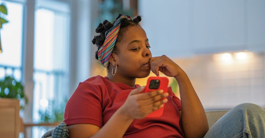 Una donna nera millenial ansiosa è seduta sul divano a casa con il telefono e si sente nervosa mentre legge notizie online o messaggi personali. Scorre lo schermo dello smartphone, stress online, tensione.