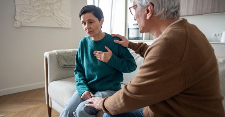 signora seduta sul divano si tiene la manu sul petto