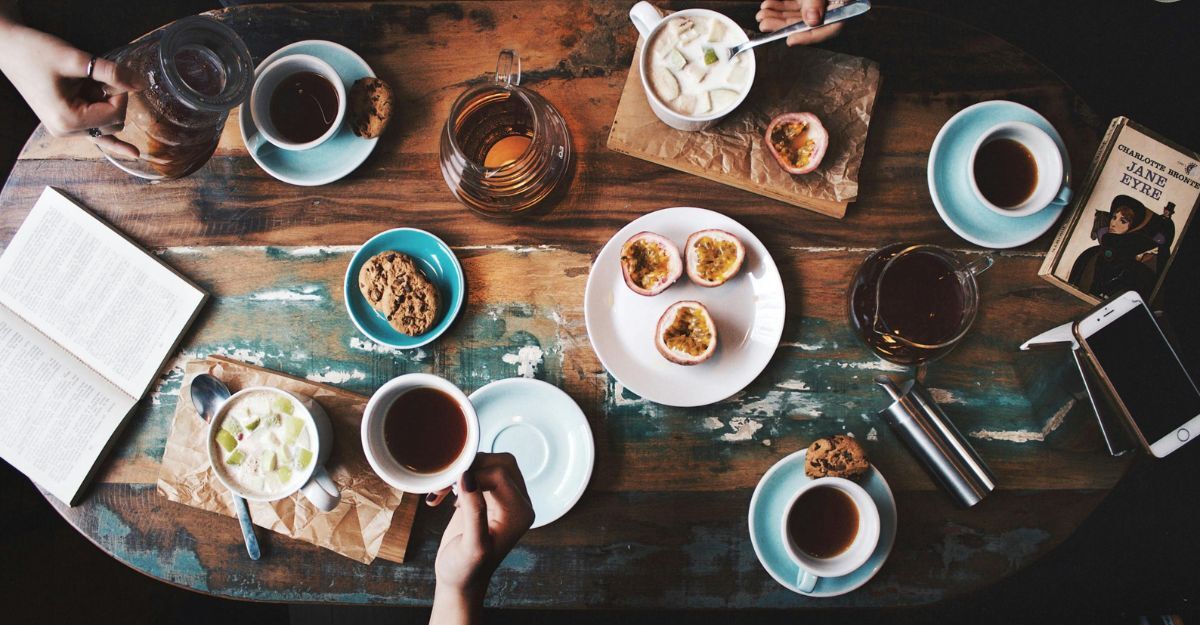 Tavolo di legno con tazze di caffè, tè, bevande cakde e fredde, mani e un libro