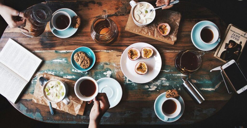 Tavolo di legno con tazze di caffè, tè, bevande cakde e fredde, mani e un libro