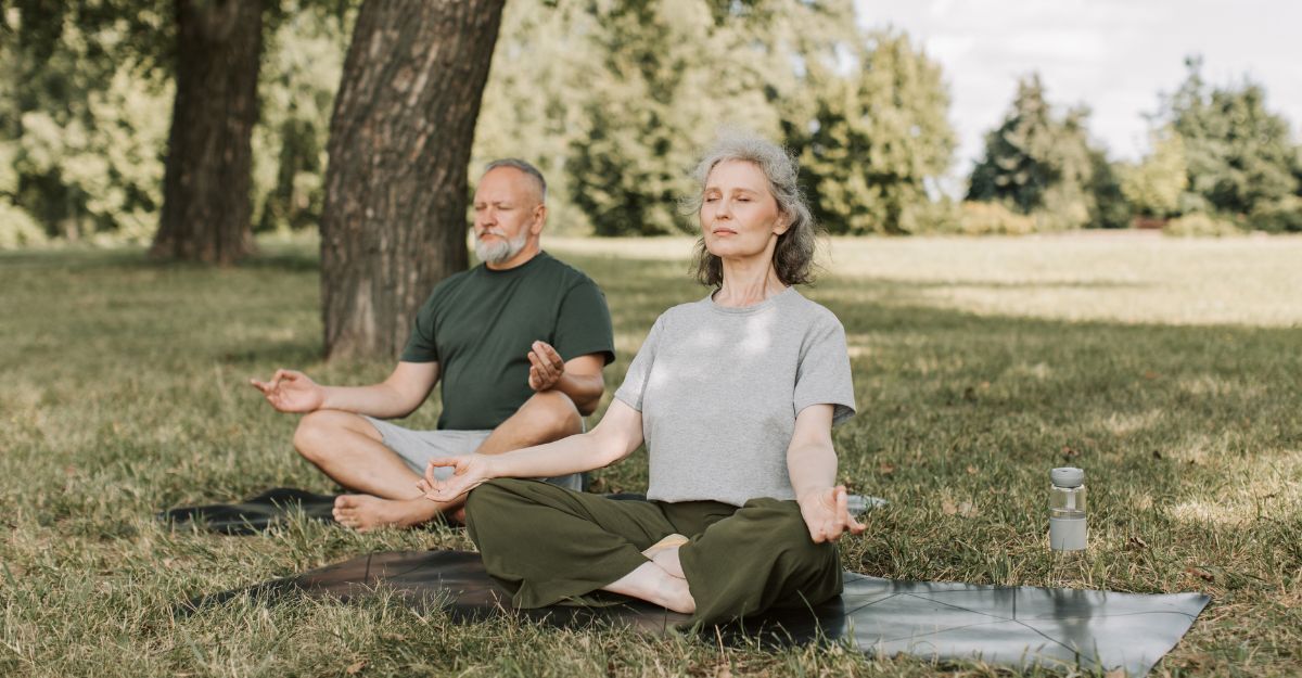 Coppia di anziani, uomo e donna, medita seduta sull'erba in un parco alberato.