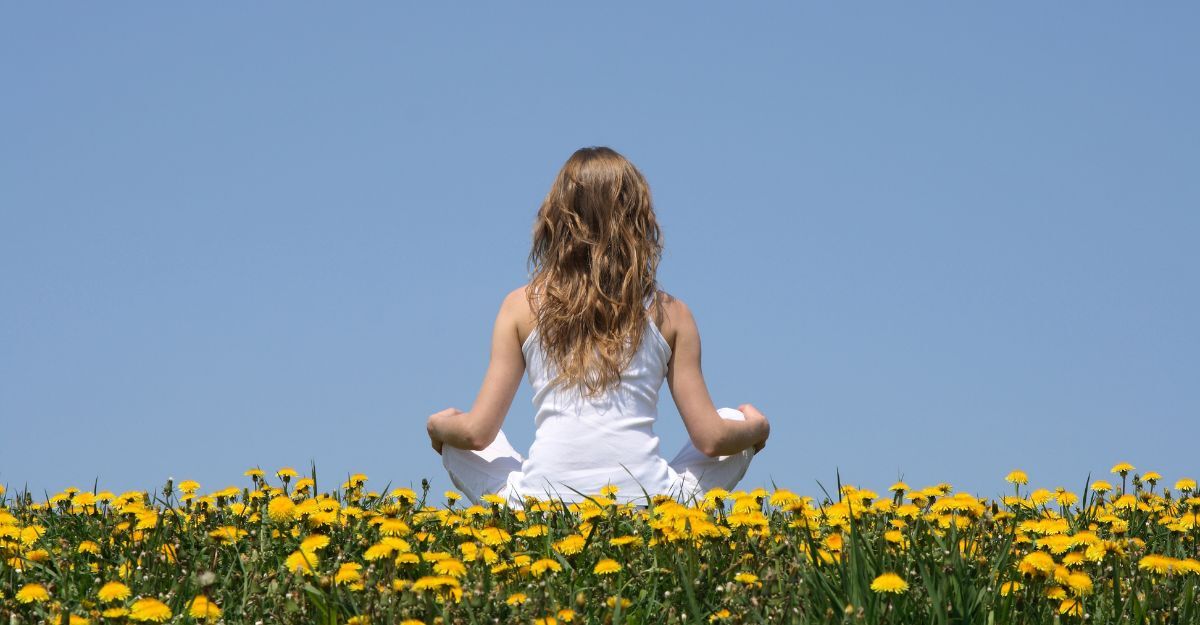 Donna dai capelli lunghi in abiti bianchi medita in posizione del loto in un campo di fiori