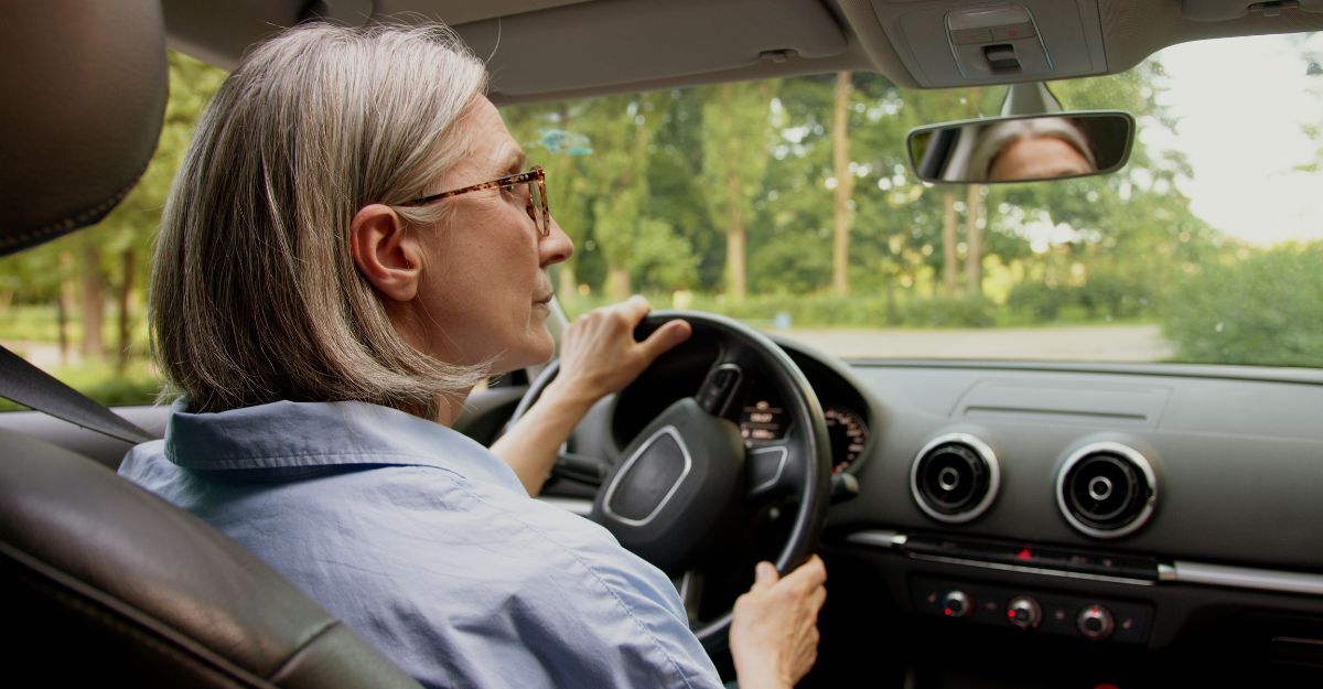 Vista posteriore di una donna d'affari caucasica matura e anziana, donna d'affari con gli occhiali, tassista, tenere il volante, sterzare, auto dentro, specchietto retrovisore, guida con attenzione, attenzione, macchina.