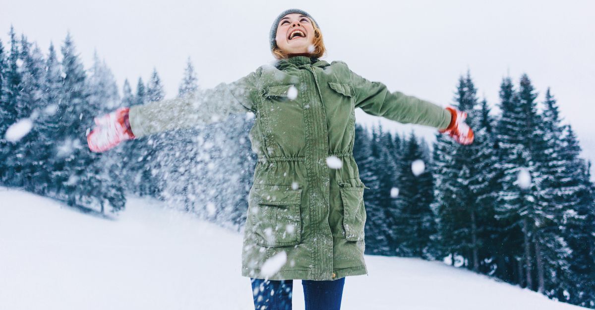 Donna felice con cappotto verde e guanti rossi nella neve