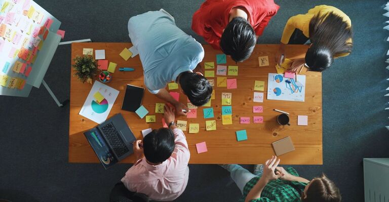 Vista dall'alto di un project manager al lavoro mentre il team di marketing supporta le sue prestazioni. Un'imprenditrice caucasica che lavora insieme a un gruppo di persone intelligenti sceglie un'idea durante una riunione.