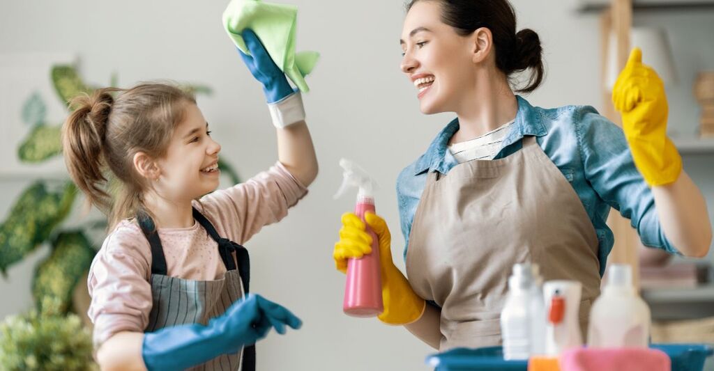 Madre e figlia sorridenti puliscono insieme, indossando guanti e grembiuli