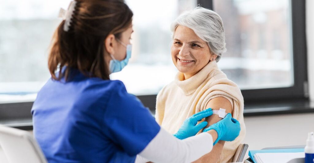 Medicina, salute e vaccinazione: medico o infermiere che applica un cerotto medico a una donna anziana vaccinata in ospedale