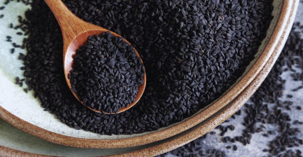 Piatto di spezie indiane. Semi di cumino nero (nigella sativa o kalonji) da vicino con un cucchiaio di legno