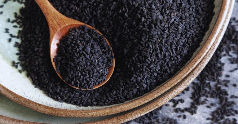 Piatto di spezie indiane. Semi di cumino nero (nigella sativa o kalonji) da vicino con un cucchiaio di legno